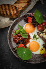 hearty breakfast - eggs with tomatoes, beans, meat, cheese and sauce on a plate
