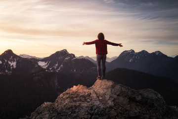 Fantasy Adventure Composite with a Girl on top of a Rock Cliff with Beautiful Nature in Background during Sunset or Sunrise. Landscape from British Columbia, Canada. Concept: Hike, Freedom, Journey