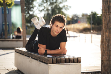 Full length portrait of handsome Caucasian man lying on bench at university campus on sunny day