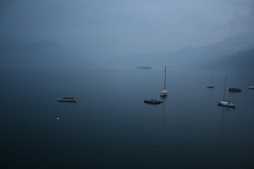 Fototapeta na wymiar Lago Maggiore in Ascona with fog mountains and sailboats 
