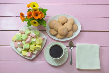 Cup of black coffee for breakfast. Marshmallows and homemade cookies on wooden pink table. Romantic table setting