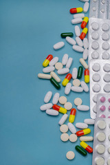 Tablets in blisters and scattered capsules of various medicines on blue background. Antibiotics and aspirin for health. Medicine and pharmacy concept
