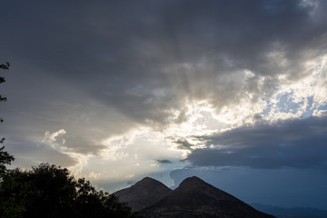 Fototapeta na wymiar Sunbeams coming out of storm clouds behind two nearly symmetrical mountains