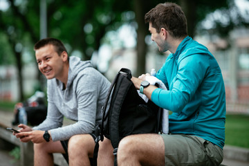 Fit young men taking rest from running. Two friends training outdoors....