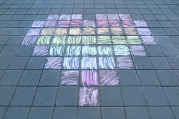 Children's drawing a heart with colored chalks on the paving tiles. Peace, kindness and love concept.
