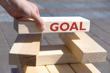 Hand of businessman holding wooden block with text GOAL over a tower of wooden blocks. Goal achievement concept.