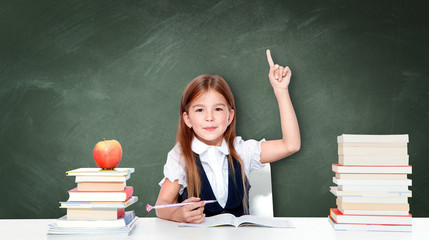 Happy and cute teen schoolgirl raising hand in classroom