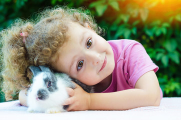 little beautiful girl smiling, hugging a baby rabbit on the green background in summer. happy laughing child and pet outdoors. bunny is a symbol of Easter. adoption. soft focus