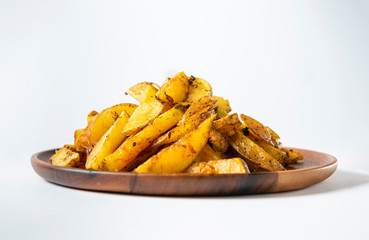 Potato wedges on wooden plate and white background. Front view.
