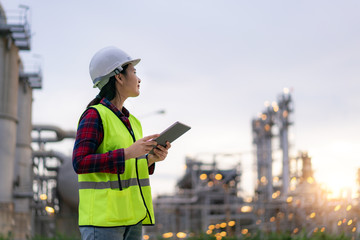 Asian woman petrochemical engineer working with digital tablet Inside oil and gas refinery plant industry factory for inspector safety quality control.. - obrazy, fototapety, plakaty