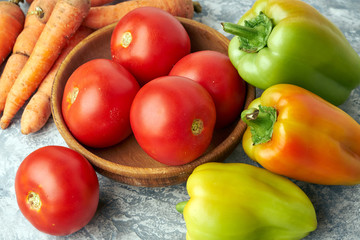 Fresh raw peppers, carrots and tomatoes in wooden bowl on gray textured background