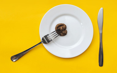 A fork strung fake plastic feces which are lie on a white plate with knife top view. The concept of an inept cook, a crappy restaurant, bad food, a taste of shit. Bad smelling joke.