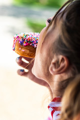 Close up of the face of a blonde woman eating a glittery sweet donut avec blended background

