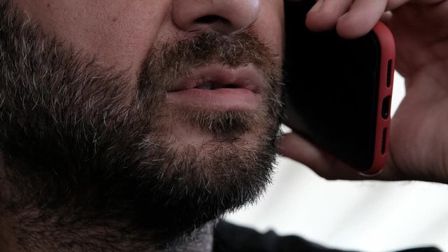 Close up portrait of bearded man talking on smart phone, focus on lips, no eyes, secret talk, criminal threatening someone
