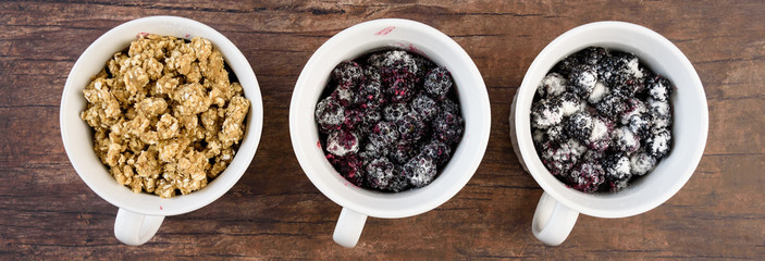 Three white single serving bowls with blackberry crumble dessert, on a wood background
