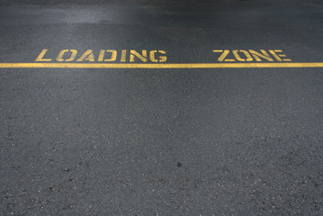 Yellow line and loading zone text on an asphalt street
