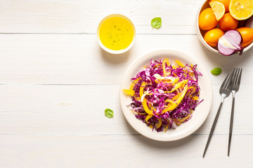 Fototapeta na wymiar Light summer salad of red cabbage, onions and yellow bell peppers, salad in a plate on a white wooden background, olive oil with spices for dressing, top view