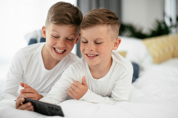 Two little brothers are playing games on the phone. Beautiful boys enjoying at home...