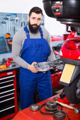 Smiling man worker fixing failed motorcycle in workshop