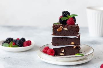 stack of chocolate brownies with hazelnuts, decorated with raspberries and blackberries. Ready for eating. Gray background. place for text.