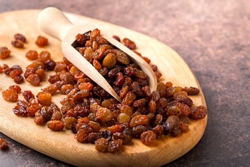Organic dried brown raisins on wooden board. Brown background, close up.