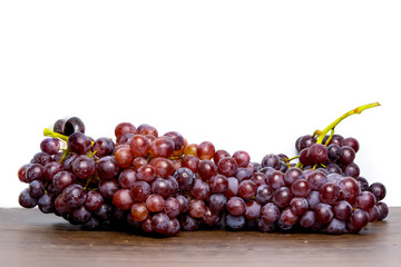 Close-up of red seedless grapes with water droplets on a wooden table and white background.