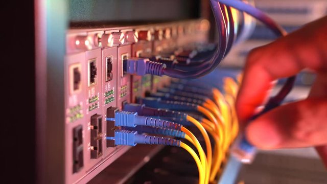 man working in network server room with fiber optic hub for digital communications and internet.