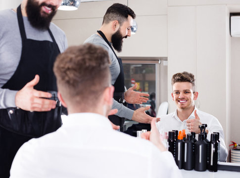 Young american male hairdresser showing resulting haircut to client at hair salon