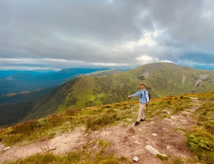Fototapeta premium The young blonde guy is in the mountains. Blue sky and beautiful nature. Fit man climb. Green trees and green grass