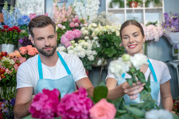 Bearded male and brown-haired female in aprons arranging flowers