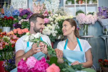 Male and female florists in aprons arranging flowers, looking at each other, smiling