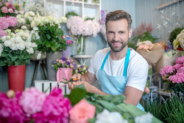 Smiling bearded florist cutting flowers inside flower shop