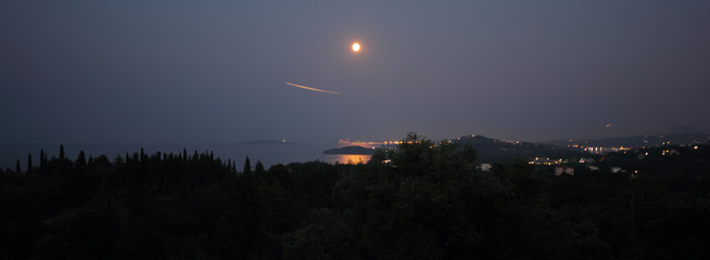Panoramic View of Full Moon Rising Over the Sea at Corfu in Greece casting a reflection of moonlight shadow on trees and island