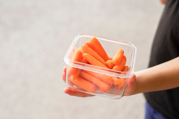 Baby carrots healthy snack container in kid's hand with empty space for text and grey background.. Healthy snack for children concept. 