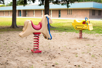 Playground near school. Kid rides in the local park playground with school building in the background.