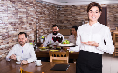 Positive young waitress greeting customers at table in restaurant