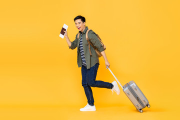 Full length portrait of cheerful young smiling tourist Asian man walking while holding luggage and...
