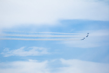 Air show, aircraft group flying leaving smoke trail with a cloudy blue sky in the background