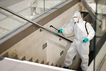 Sanitation worker in hazmat suit disinfecting public passages during COVID-19 pandemic.