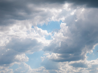 Sun rays breaking through a large cloud formed in the sky surrounded by diffuse clouds and a blue sky in the background