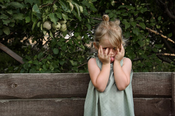 Little girl shows tongue and hides her face with her hands