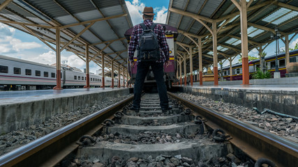 Fototapeta na wymiar A young man standing on a train track at Chiang Mai Railway Station, Thailand with a back view.