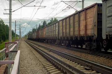 Fototapeta na wymiar Locomotive with freight cars rides on the railway along the forest