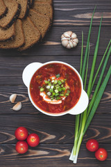 Homemade tomato soup with rye bread and garlic on a dark wooden table. Beetroot soup in a bowl with sour cream and green onions. Russian traditional cuisine. The national Ukrainian dish is borscht.