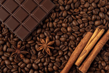 Chocolate bar with star anise and cinnamon on coffee grains background. Top view. Flat lay. Copy space.