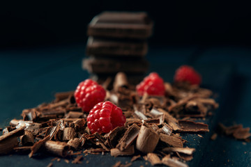 Chocolate pieces with chocolate shavings and raspberry on dark wooden background