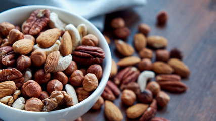 Wooden bowl with mixed nuts on table top view. Healthy food and snack. Walnut, pistachios, almonds, hazelnuts and cashews.