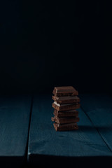 Heap of chocolate pieces on dark blue wooden table. Copy space.