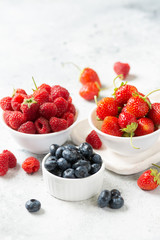 Ripe berries. Different berries in white ceramic bowls on a light table. Strawberries, raspberries and blueberries in plates. Space for text