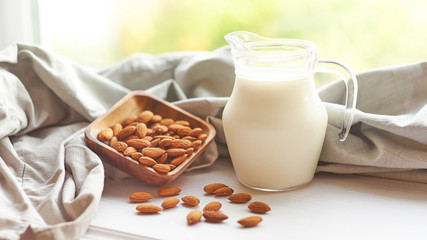 Almond milk in glass with almonds in wooden bowl on a white wooden table